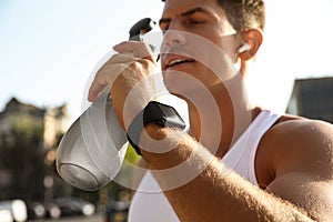 Man with fitness tracker drinking water after training outdoors, closeup