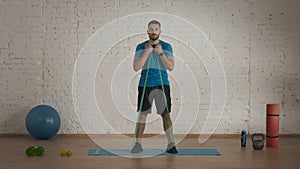 Man fitness trainer in sportswear doing biceps pulling exercise with elastic band for online class at the home.