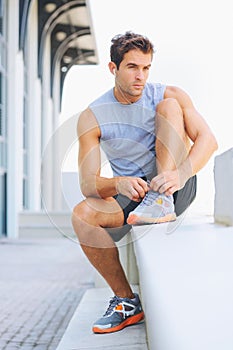 Man, fitness and tying shoes getting ready for workout, exercise or outdoor training with earphones. Active male person