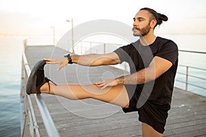 Man in fitwear performs standing leg stretch on pier outdoors