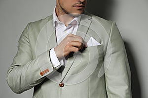 Man fixing handkerchief in breast pocket of his suit on grey