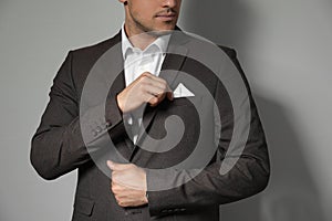 Man fixing handkerchief in breast pocket of his suit on light grey background, closeup