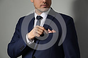 Man fixing handkerchief in breast pocket of his suit on light grey background, closeup