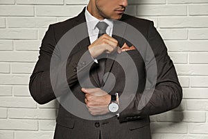 Man fixing handkerchief in breast pocket of his suit near white brick wall