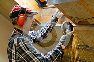 Man fixing metal frame using angle grinder on attic ceiling covered with rock wool