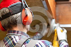 Man fixing metal frame using angle grinder on attic ceiling covered with rock wool