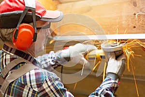 Man fixing metal frame using angle grinder on attic ceiling covered with rock wool