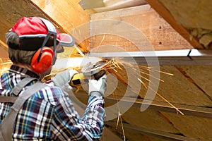 Man fixing metal frame using angle grinder on attic ceiling covered with rock wool