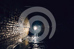 Man with flashlight in dark dirty brick underground tunnel or sewerage corridor