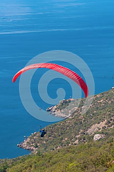 A man flies on a paraglider over a mountain in greenery and a blue sea