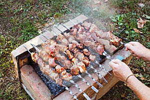 A man flips pork skewers grilled over coals on a brick grill. Delicious weekend barbecue