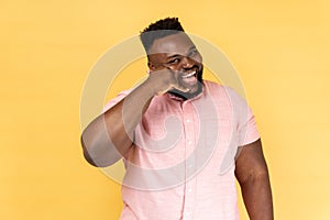 Man flirting holding fingers near ear showing call gesture with toothy smile, answering call.