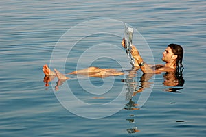 Man floating in a dead sea with newspaper