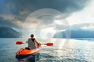 Man floating on kayak under sunrise sky on Cheow Lan Lake, Khao Sok national park, Thailand