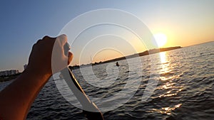 Man floating white SUP board paddles rowing oar POV dawn sunset sea surface wave