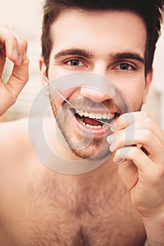 Man is flossing his teeth in bathroom in morning.