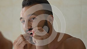 Man flossing his teeth in front of mirror in bathroom, dental care, oral hygiene