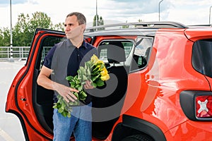 A man with flowers in his hands stands near a car