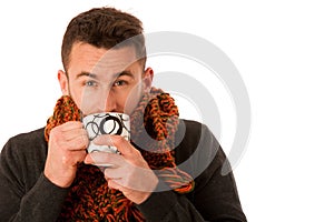 Man with flu and fever wrapped in scarf holding cup of healing t