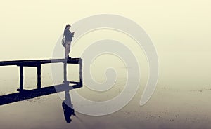 Man with fly-fishing gear catching a trout from jetty on a foggy morning