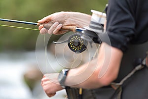 Man fly fishing with reel and rod. Sport fly fisher man close up on reel.