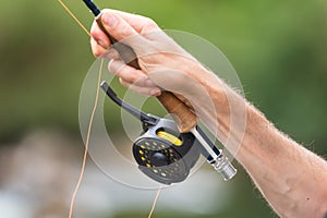 Man fly fishing with reel and rod. Sport fly fisher man close up on reel.