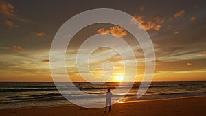 A man flying drone in bright yellow sunset on the beach.