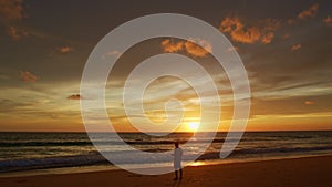 A man flying drone in bright yellow sunset on the beach.