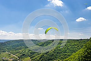 Man flying a green paraglider over beautiful wineries in Germany, visible river and forest.