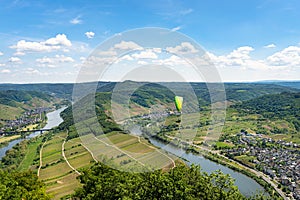 Man flying a green paraglider over beautiful wineries in Germany, visible river and forest.