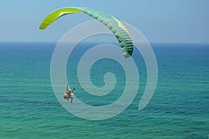 Man is flying on green paraglider in the sky above the azure sea. Balance, extreme sports, lifestyle. Mediterranean Sea Israel