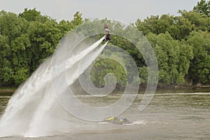 Man Flying on Jetpack Over Scenic River with Green Trees on Riverbank Under Clear Blue Sky on a Beautiful Sunny Day, Experiencing