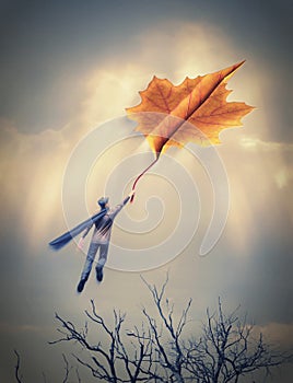 Man flying with a leaf. Man flies on the last autumn leaf to the sky. Maple leaf folded like a paper plane in storm sky. Freedom
