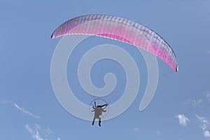 Man flying motorized parasail in blue sky with small puffy clouds