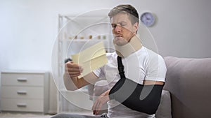 Man in foam cervical collar and arm sling opening envelope with bill, high price