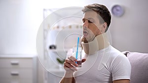Man in foam cervical collar trying to drink glass water with straw, poor attempt