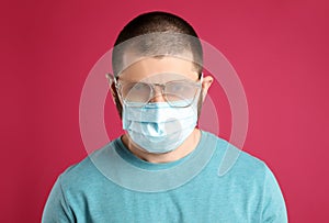 Man with foggy glasses caused by wearing disposable mask on pink background. Protective measure during coronavirus pandemic