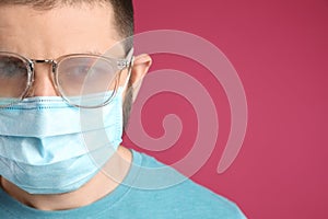 Man with foggy glasses caused by wearing disposable mask on pink background, space for text. Protective measure during coronavirus