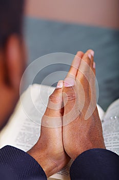 Man folding hands praying with open bible lying in front, seen from behind models head, religion concept