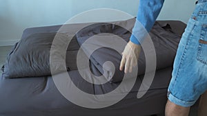Man folds the blanket and pillow and tucks in the sofa, closeup view