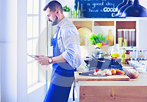 Man following recipe on digital tablet and cooking tasty and healthy food in kitchen at home