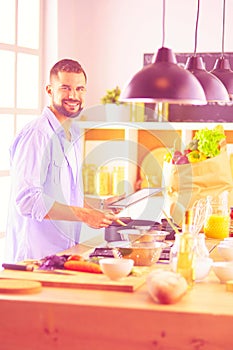 Man following recipe on digital tablet and cooking tasty and healthy food in kitchen at home