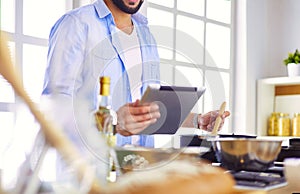 Man following recipe on digital tablet and cooking tasty and healthy food in kitchen at home