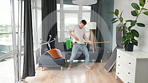 Man fooling around while cleaning the house and imagines himself a rock star