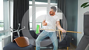 Man fooling around while cleaning the house and imagines himself a rock star, plays the broom like a guitar. Slow motion