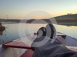 Man foot on traditional wood boat at calm lake with dramatic sunrise colorful sky reflection