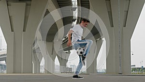 Man footballer is practicing kicks tricks with ball in city under the bridge.