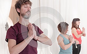 The man in the foreground with the hands in Namaste`s gesture. Close up of man meditating at yoga studio.