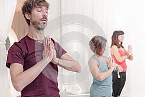 The man in the foreground with the hands in Namaste`s gesture. Close up of man meditating at yoga studio.