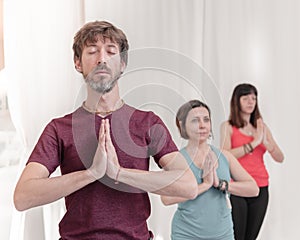The man in the foreground with the hands in Namaste`s gesture. Close up of man meditating at yoga studio.